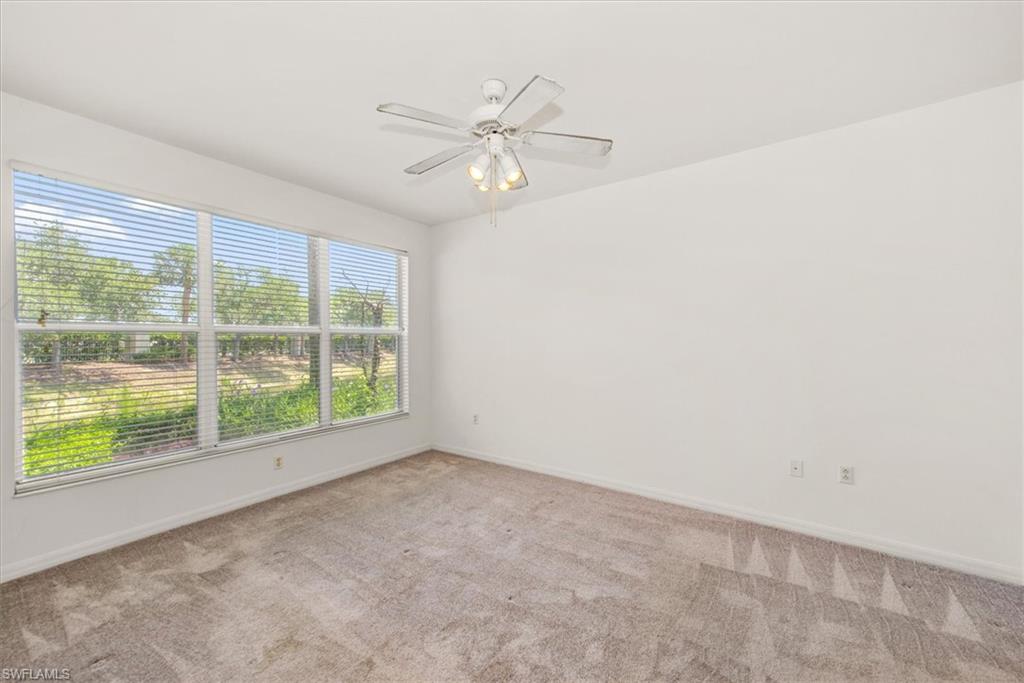 Spacious room featuring a multi-pane window with horizontal blinds, neutral-toned carpeting, white walls, and a ceiling fan with integrated lighting