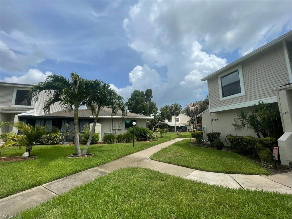 Exterior property featuring a concrete walkway, lush green lawn, mature palm trees, and established shrubbery