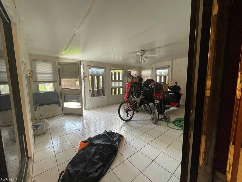 Enclosed patio space featuring white square tile flooring, multiple windows providing ample natural light, and a ceiling fan with integrated lighting