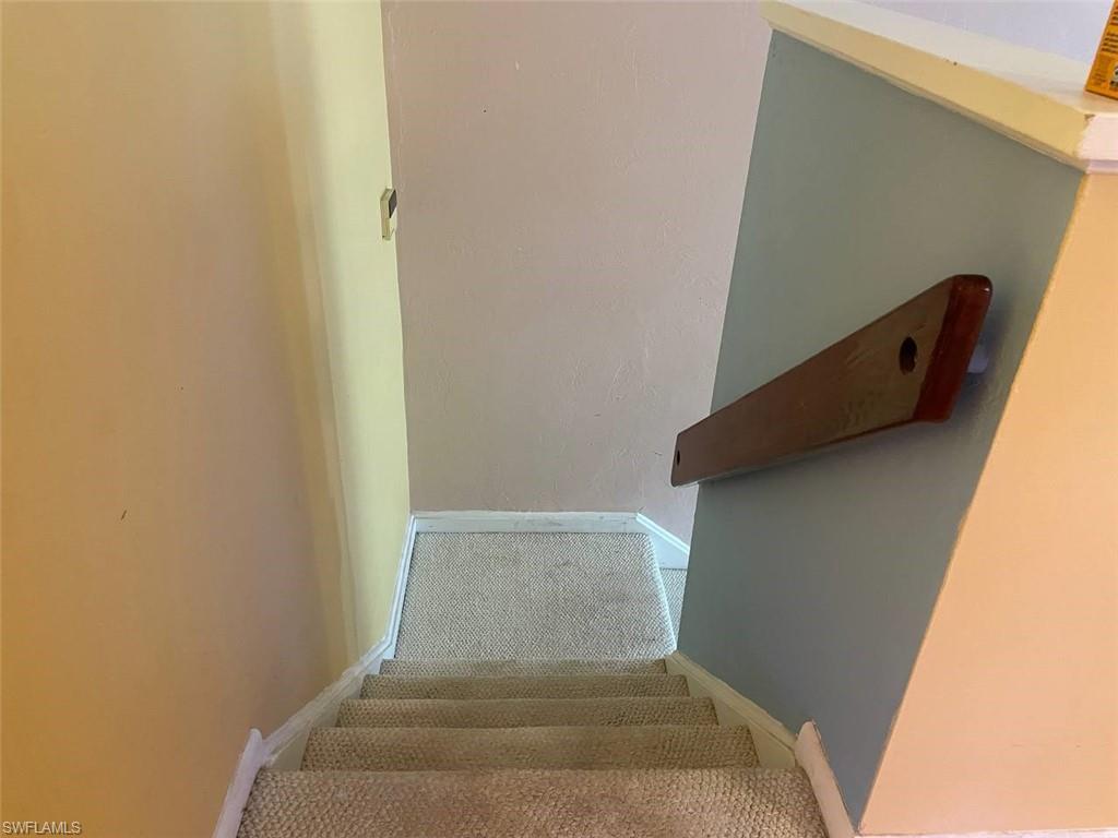 Carpeted staircase with white trim, featuring a dark wood-finish wall-mounted handrail