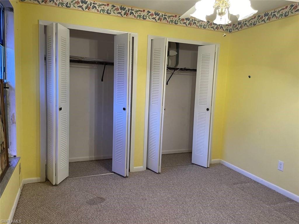 Carpeted interior space featuring two bi-fold louvered closet doors, wall-mounted light fixture, and decorative wallpaper border
