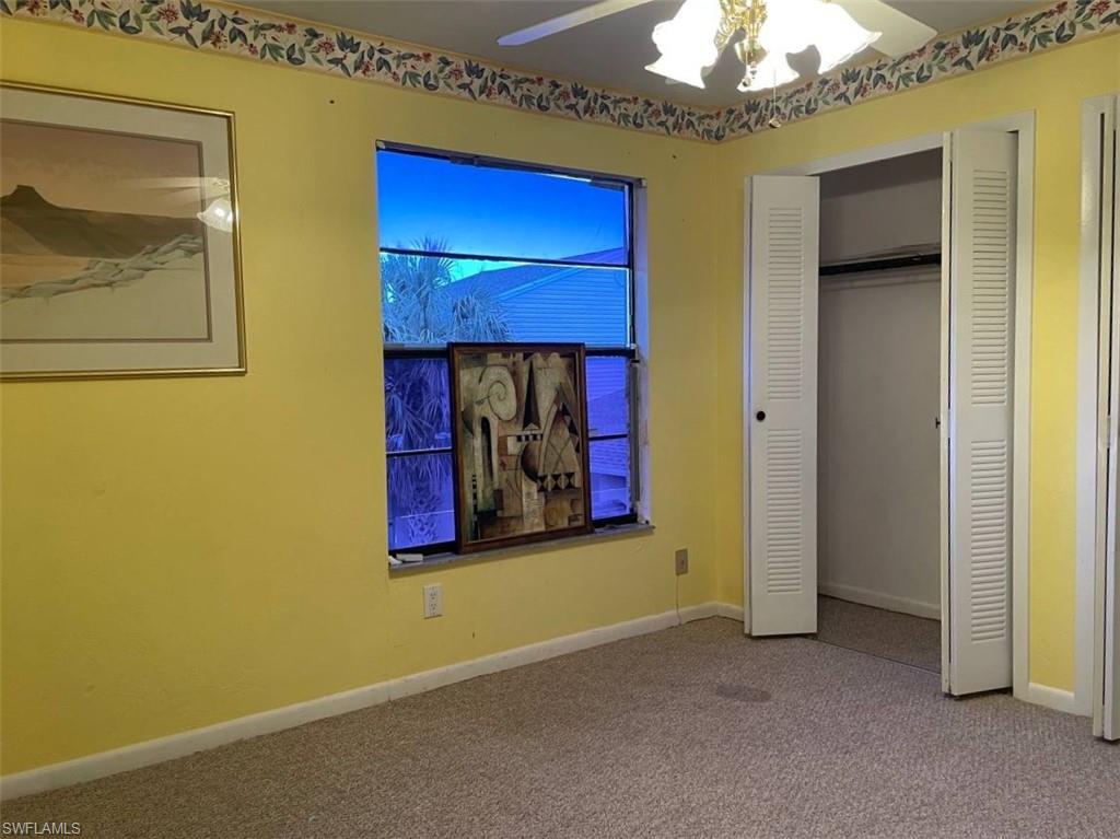 Carpeted room featuring a window with exterior visibility, louvered bi-fold closet doors, and a ceiling fan with integrated lighting
