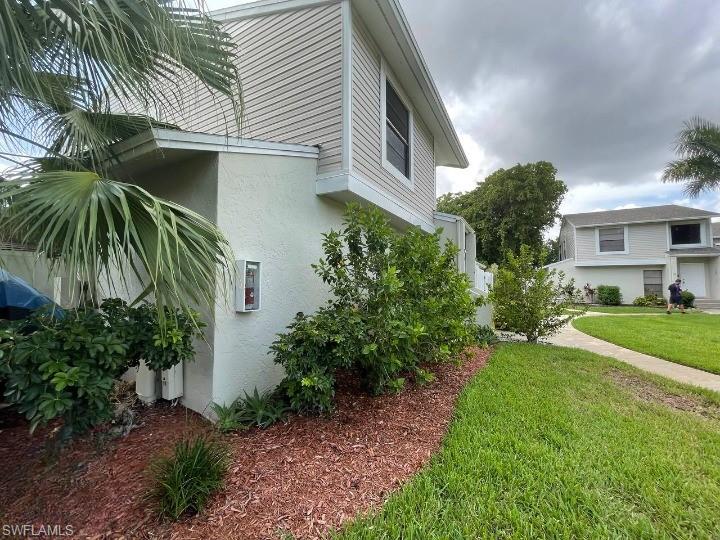 Exterior featuring light stucco and horizontal siding, with an established landscape bed, mature palm foliage, and a concrete pathway