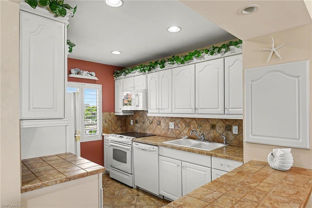 KITCHEN W/TILED COUNTERTOPS AND FULL-HEIGHT TILED BACKSPLASH WITH DECORATIVE TILE INSERTS.  PLANTATION SHUTTER DRESSES IMPACT RESISTANT WINDOW.  RECESSED LIGHTING.