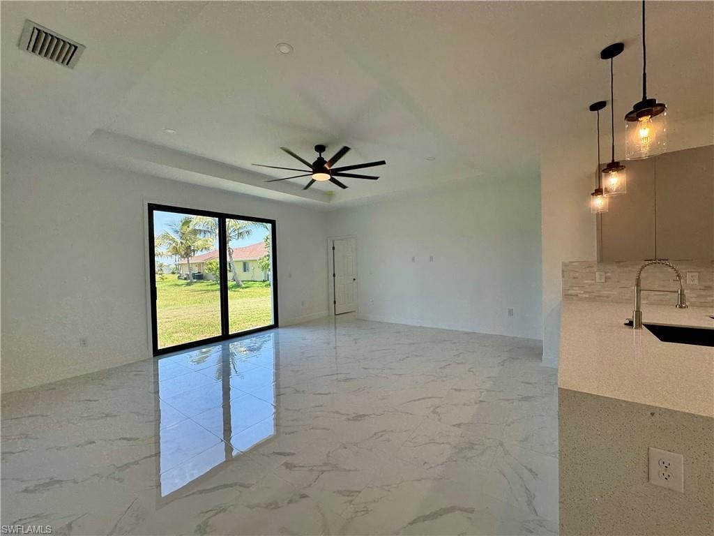 Tiled empty room with sink, ceiling fan, and a tray ceiling