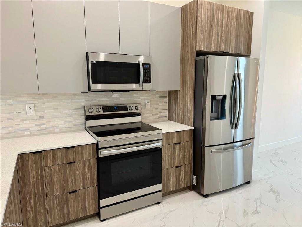 Kitchen featuring backsplash, appliances with stainless steel finishes, and light tile flooring
