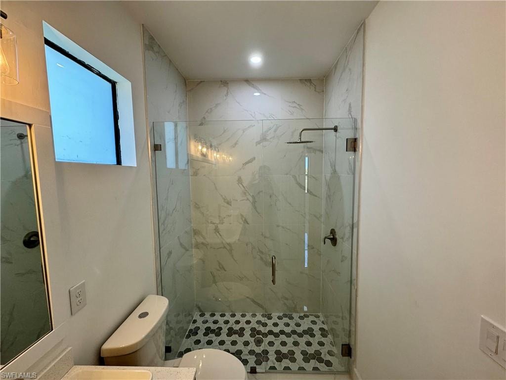 Bathroom featuring a shower with door and toilet
