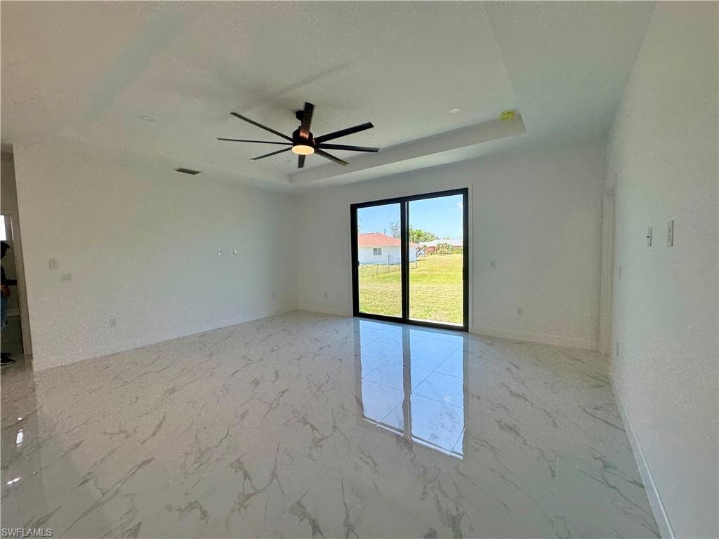 Unfurnished room with ceiling fan, a tray ceiling, and light tile floors