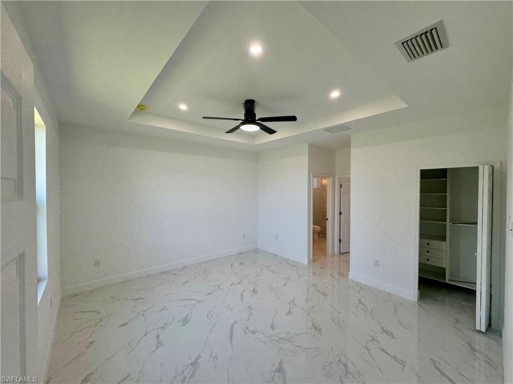 Unfurnished bedroom with a closet, ceiling fan, a tray ceiling, and light tile flooring