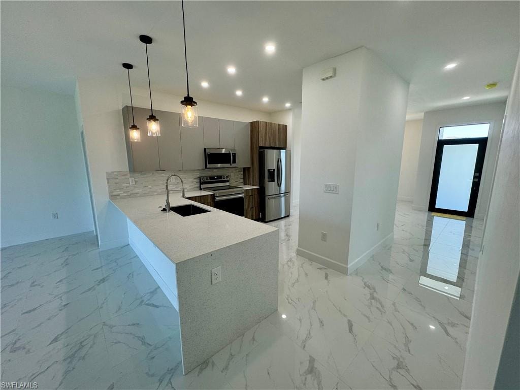 Kitchen featuring stainless steel appliances, backsplash, light tile floors, hanging light fixtures, and sink