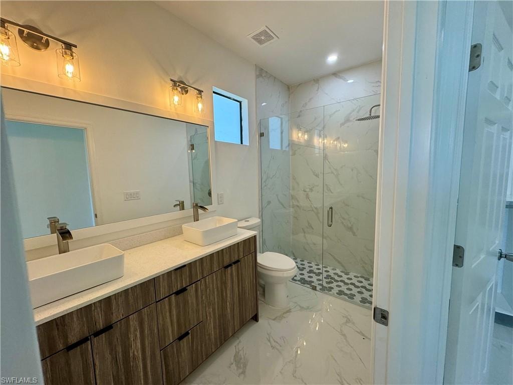 Bathroom featuring tile floors, walk in shower, double sink vanity, and toilet