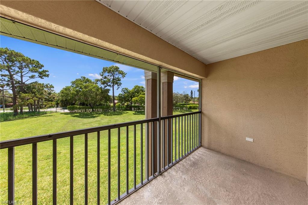 Screened balcony featuring a textured wall, white soffit ceiling, and black metal railings overlooking a landscaped green space with mature trees