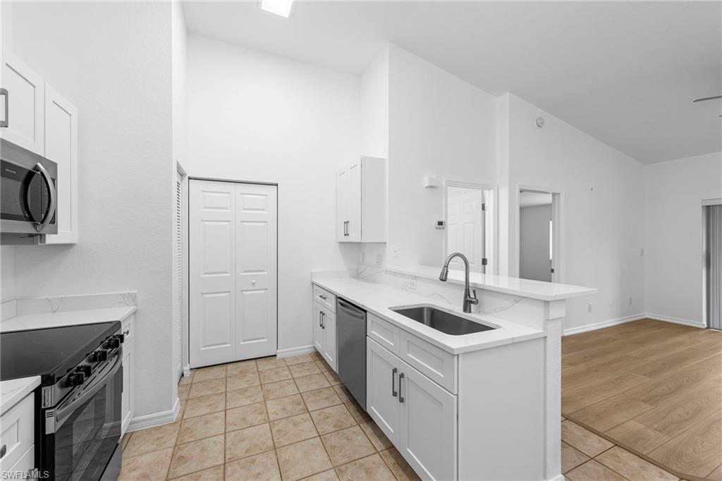 Modern kitchen featuring white shaker cabinetry, stainless steel appliances, a single-basin sink with a gooseneck faucet, light-toned countertops, and tile flooring