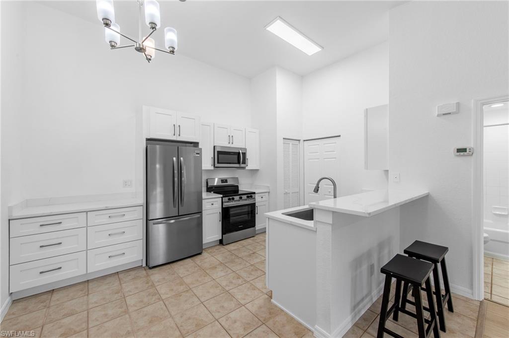 Modern kitchen featuring stainless steel appliances, white cabinetry, a bar-height countertop, a stainless steel sink, and tile flooring