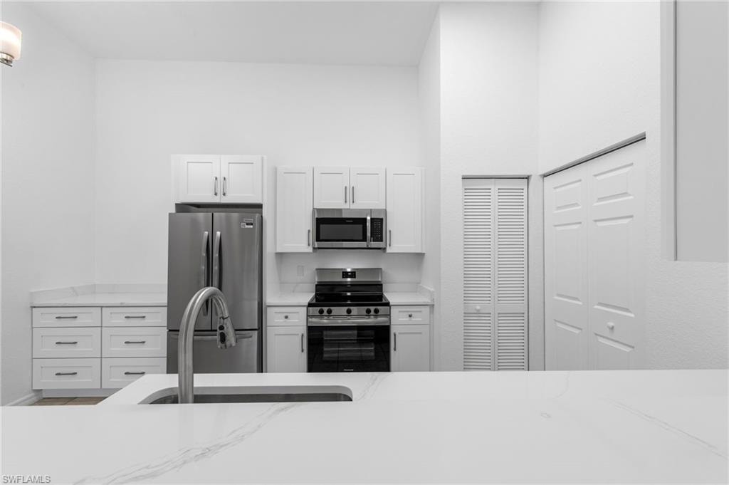 Modern kitchen featuring white shaker cabinetry, stainless steel appliances, white countertops, and a prominent kitchen island with an undermount sink