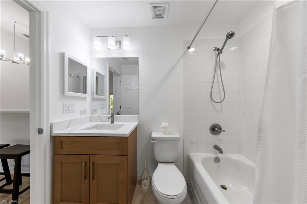 Bathroom featuring a wood-finish vanity with a white countertop, an undermount sink, a large wall mirror, and a tiled tub/shower combination