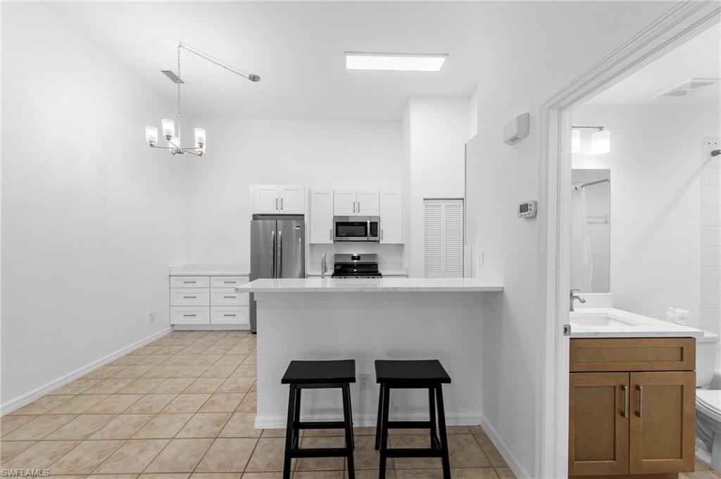 Open-concept kitchen featuring white cabinetry, stainless steel appliances, and a breakfast bar with a light-toned countertop