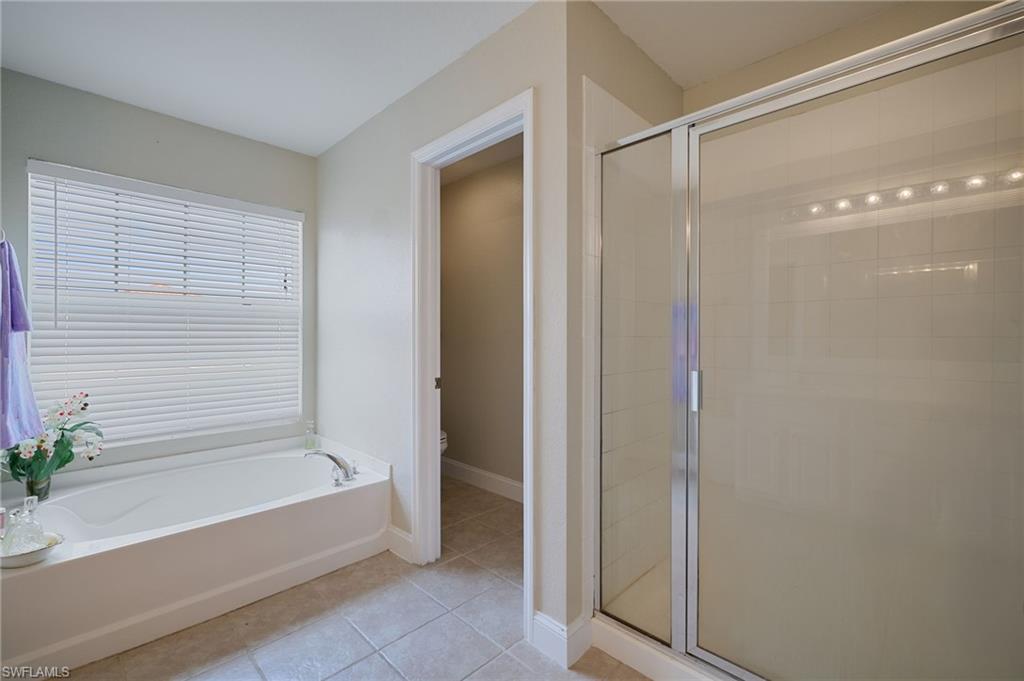 Bathroom featuring a built-in tub, separate shower with frosted glass enclosure, tile flooring, and a window with horizontal blinds