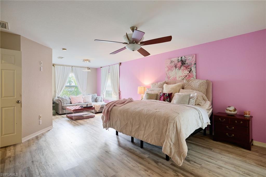Open-concept room featuring wood-finish flooring, a ceiling fan with integrated lighting, and multiple windows with vertical blinds