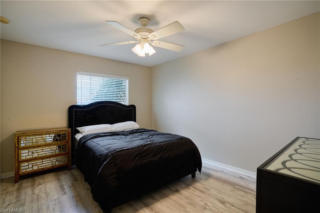 Light-toned walls with a single window featuring blinds, wood-finish flooring, and a ceiling fan with integrated lighting
