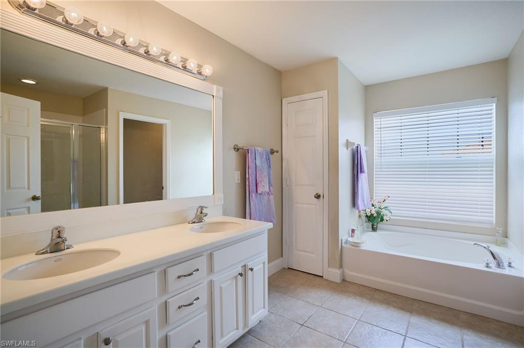 Bathroom featuring a dual vanity with white cabinetry, a built-in bathtub with window, a large wall-mounted mirror, and tile flooring