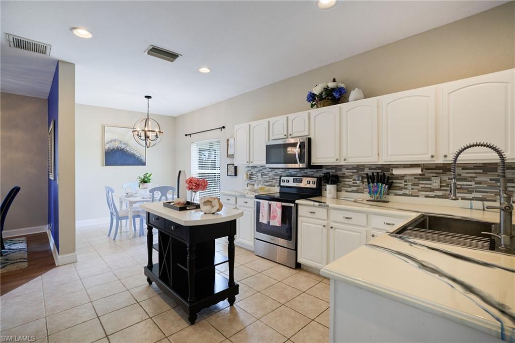 Kitchen with white cabinetry, stainless steel appliances, a multi-tone tile backsplash, and light-toned tile flooring