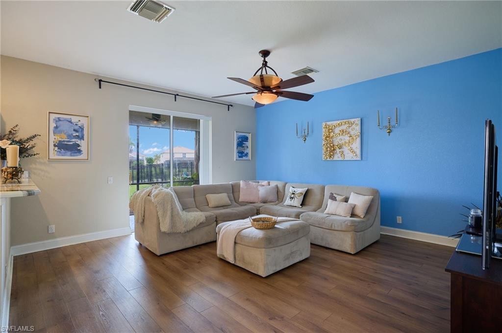 Open-concept living space featuring wood-finish flooring, a ceiling fan with integrated lighting, and a prominent accent wall