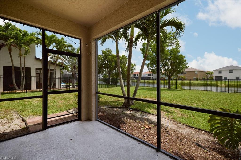 Screened patio with concrete flooring offering expansive lawn space, mature palm trees, and a water feature beyond the rear fencing