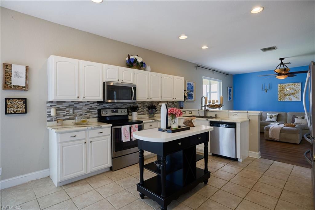Open-concept kitchen featuring white cabinetry, stainless steel appliances, a tile backsplash, and a movable kitchen island