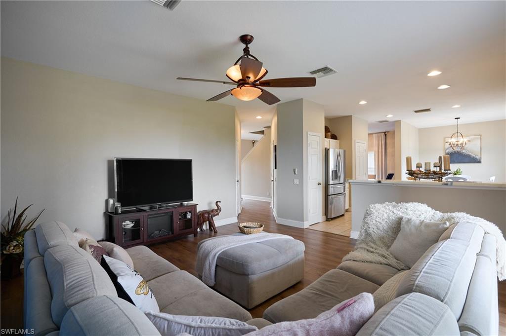 Open-concept living area featuring wood-finish flooring, a ceiling fan with integrated lighting, recessed lighting, a half-wall partition, and neutral wall tones