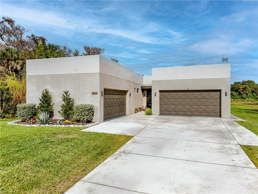 Modern exterior architecture with a two-tone facade, featuring two wood-finish garage doors, a concrete driveway, and established landscaping beds
