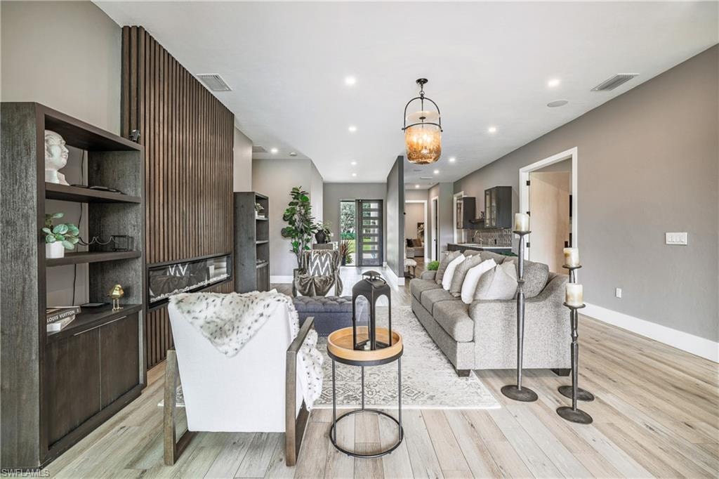 Open-concept living space with light wood-finish flooring, recessed lighting, and a contemporary fireplace feature wall