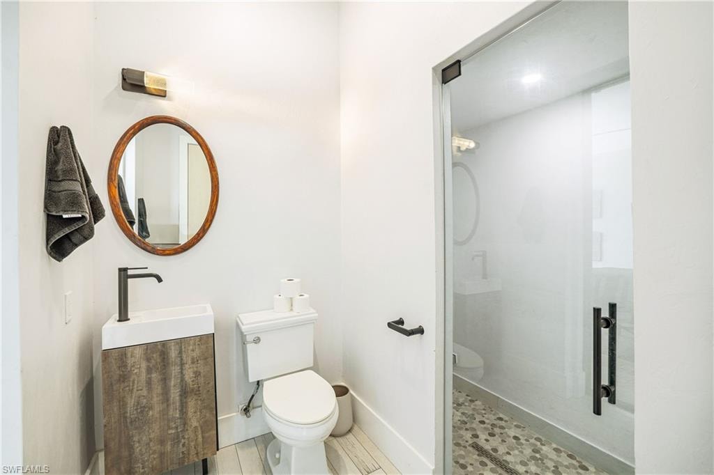 Modern bathroom featuring a glass-enclosed shower with pebble-tile flooring, a wood-finish vanity with a vessel sink, a matte black faucet, and a round wooden mirror
