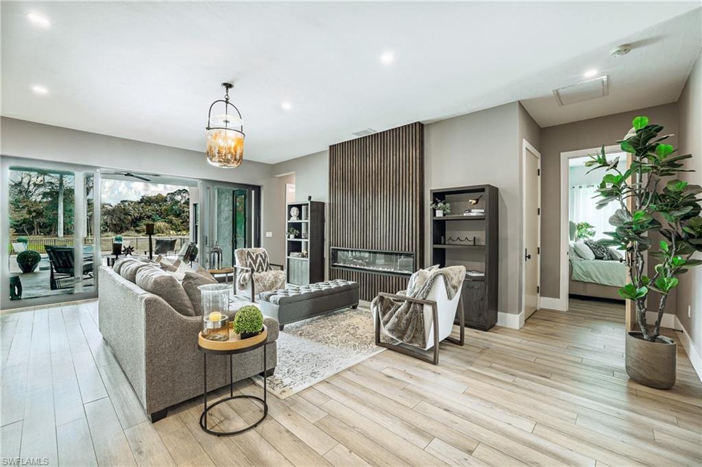Spacious living area featuring light wood-finish flooring, a wall-mounted linear fireplace with vertical slat paneling, and a contemporary chandelier