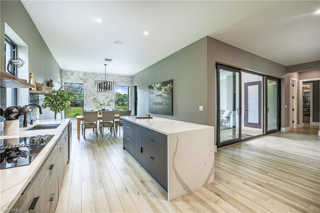 Contemporary kitchen and dining area featuring light wood-finish flooring, a waterfall edge kitchen island with integrated cabinetry, and stone-look accent wall