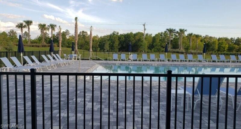 Community swimming pool featuring a paver patio surround, black metal fencing, and perimeter landscaping