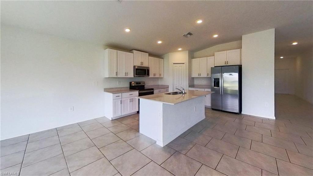 Contemporary kitchen featuring white cabinetry, a central island with an integrated sink, stainless steel appliances, recessed lighting, and tile flooring
