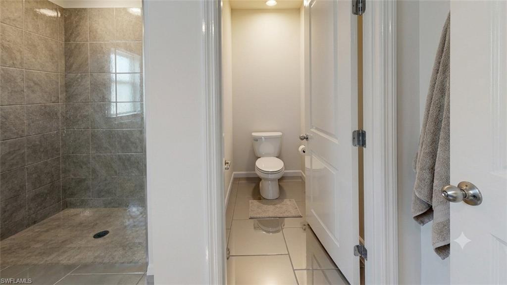 Bathroom featuring a fully tiled shower with a window, a separate toilet area with recessed lighting, and large format floor tiles
