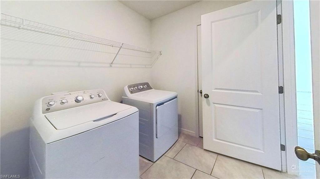 Laundry area featuring light-toned walls, tile flooring, and overhead wire shelving