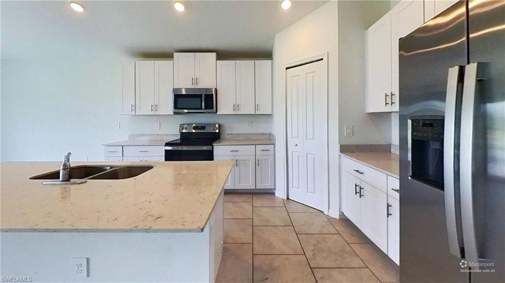 Kitchen featuring a central island with an undermount dual-basin sink, light-toned countertops, white cabinetry with dark hardware, stainless steel appliances, and tiled flooring