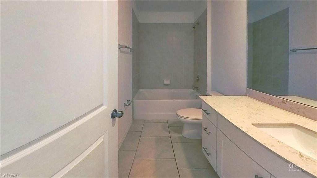 Full bathroom featuring a white vanity with an undermount sink, a light-toned countertop, a large wall-mounted mirror, and a combined tub and shower with tile surround
