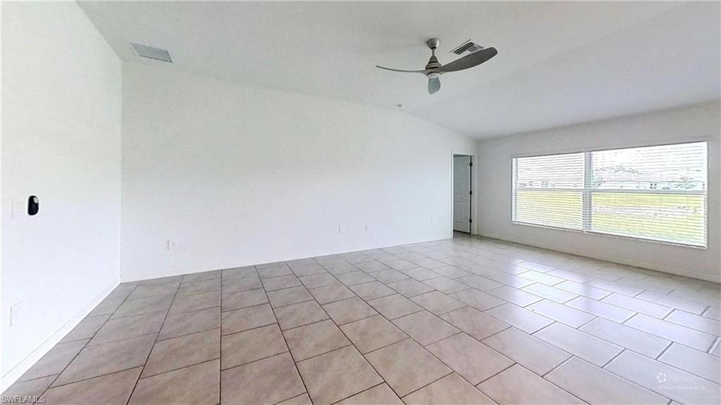 Spacious room featuring neutral tile flooring, vaulted ceilings, and a ceiling fan
