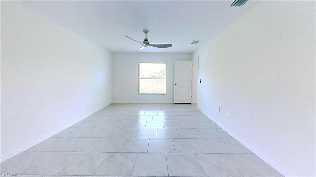 Spacious room featuring light-toned tile flooring, a window providing natural light, a ceiling fan, and white baseboards