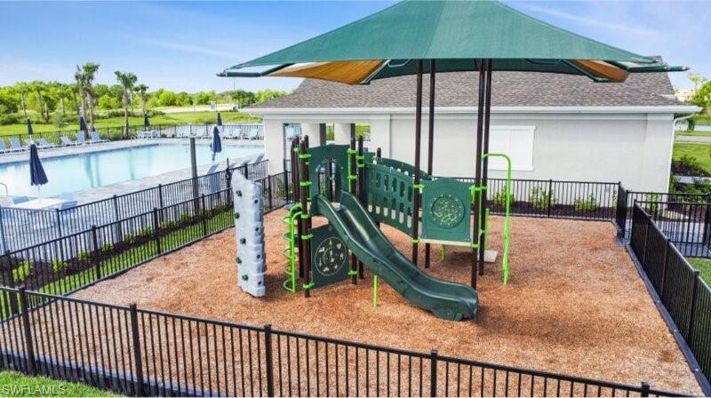 Outdoor recreational area featuring a playground with a slide and climbing wall, covered by a green shade structure