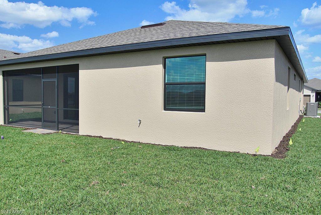 Expansive backyard featuring a screened patio, stucco exterior, asphalt shingle roof, and a visible exterior air conditioning unit
