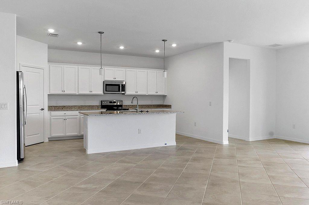 Open-concept kitchen featuring white cabinetry, stainless steel appliances, granite countertops, and a central island with pendant lighting