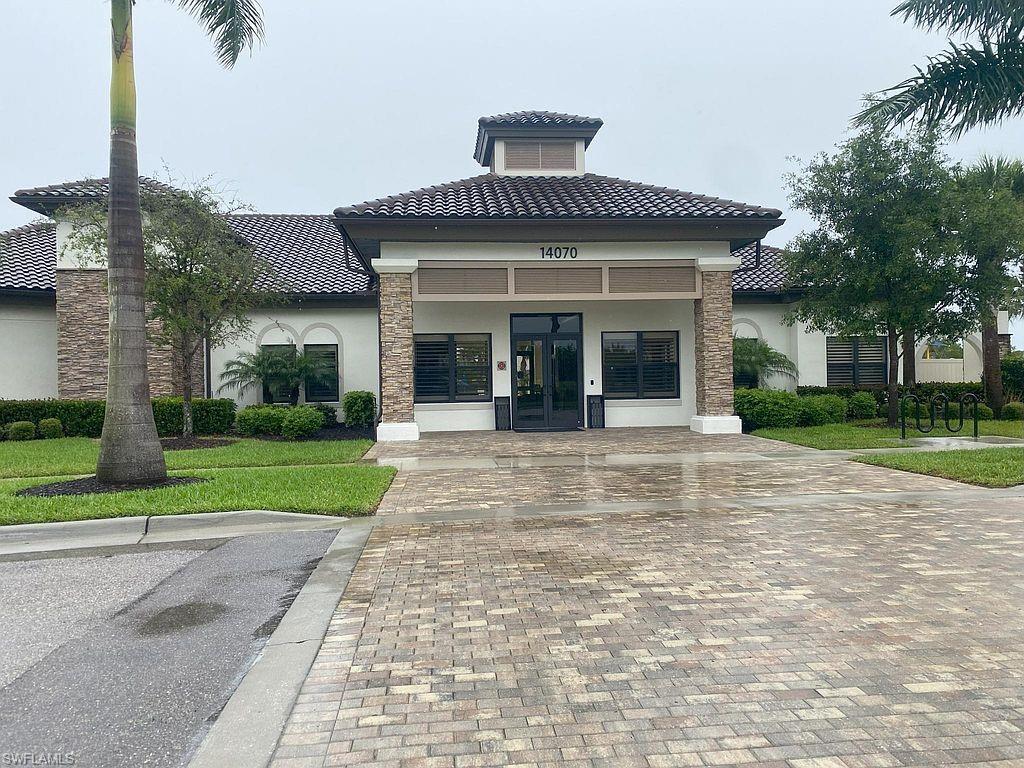 Mediterranean-inspired architectural style featuring a tiled roof, stone veneer accents, stucco exterior, black-framed windows, and a paver driveway