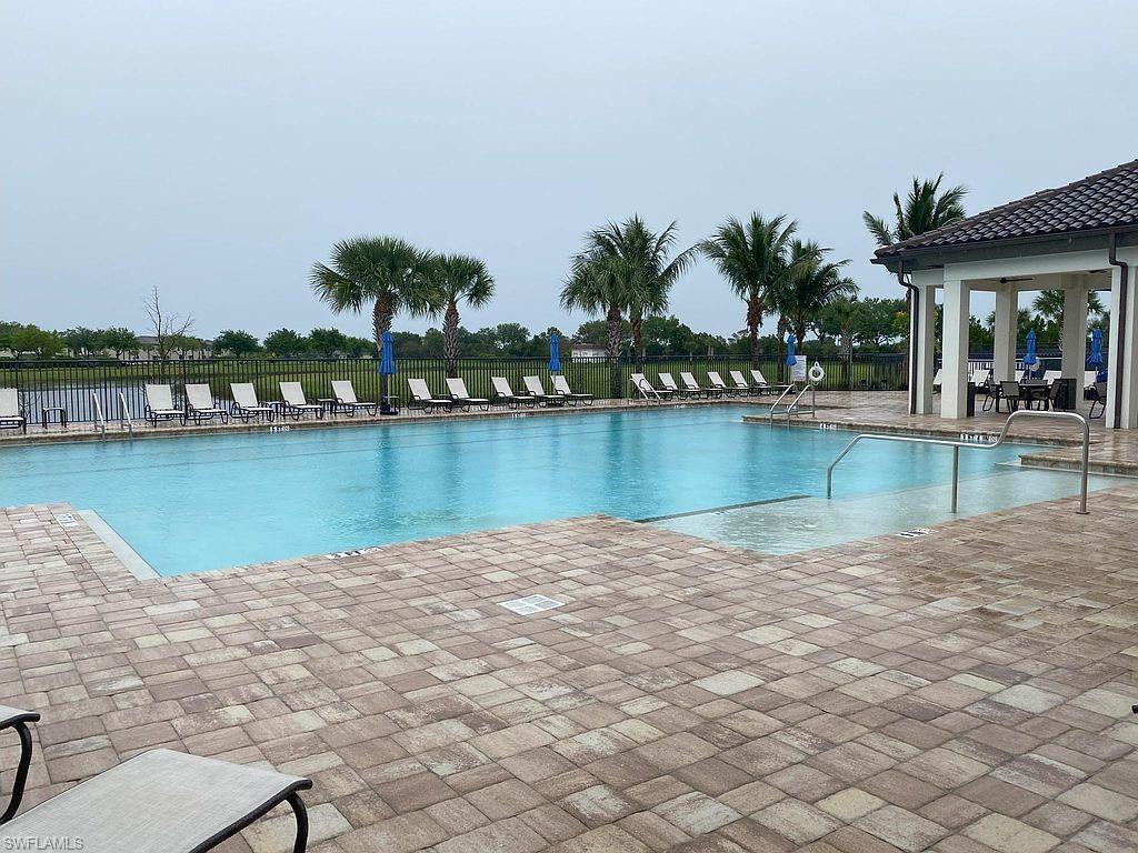 Large rectangular swimming pool surrounded by paver decking, featuring a covered cabana with tile roof and columns