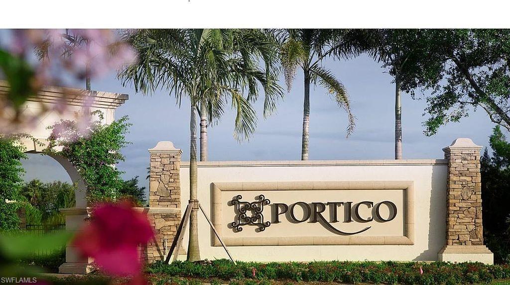 Community entrance sign featuring a decorative archway with climbing foliage, stone-clad pillars, palm trees, and manicured landscaping