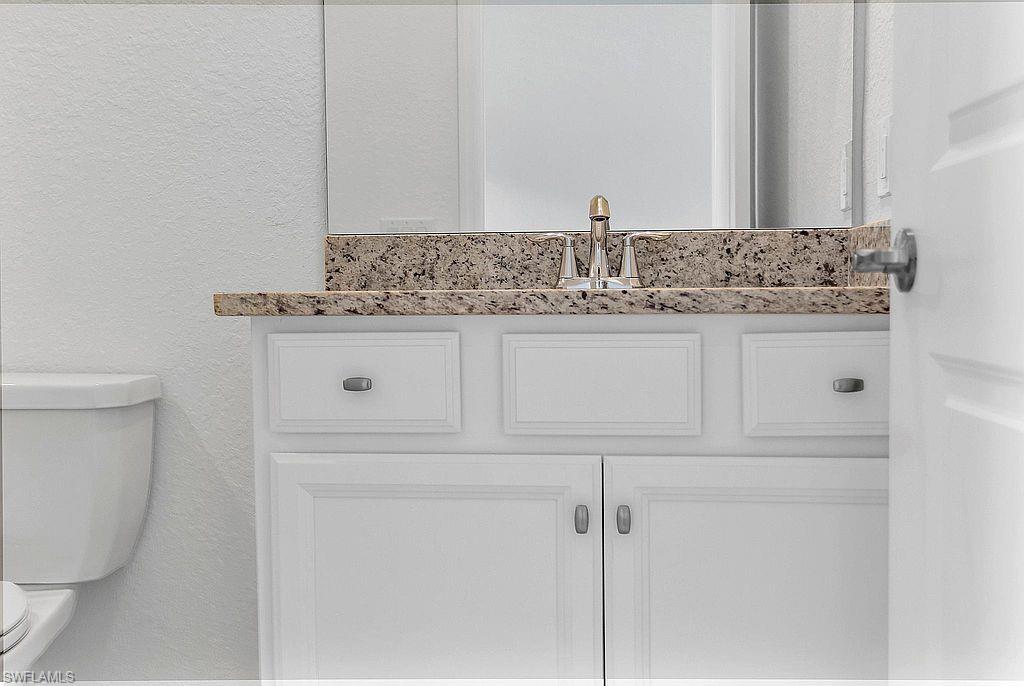 Bathroom vanity featuring a speckled countertop, white cabinetry with silver hardware, and a chrome faucet
